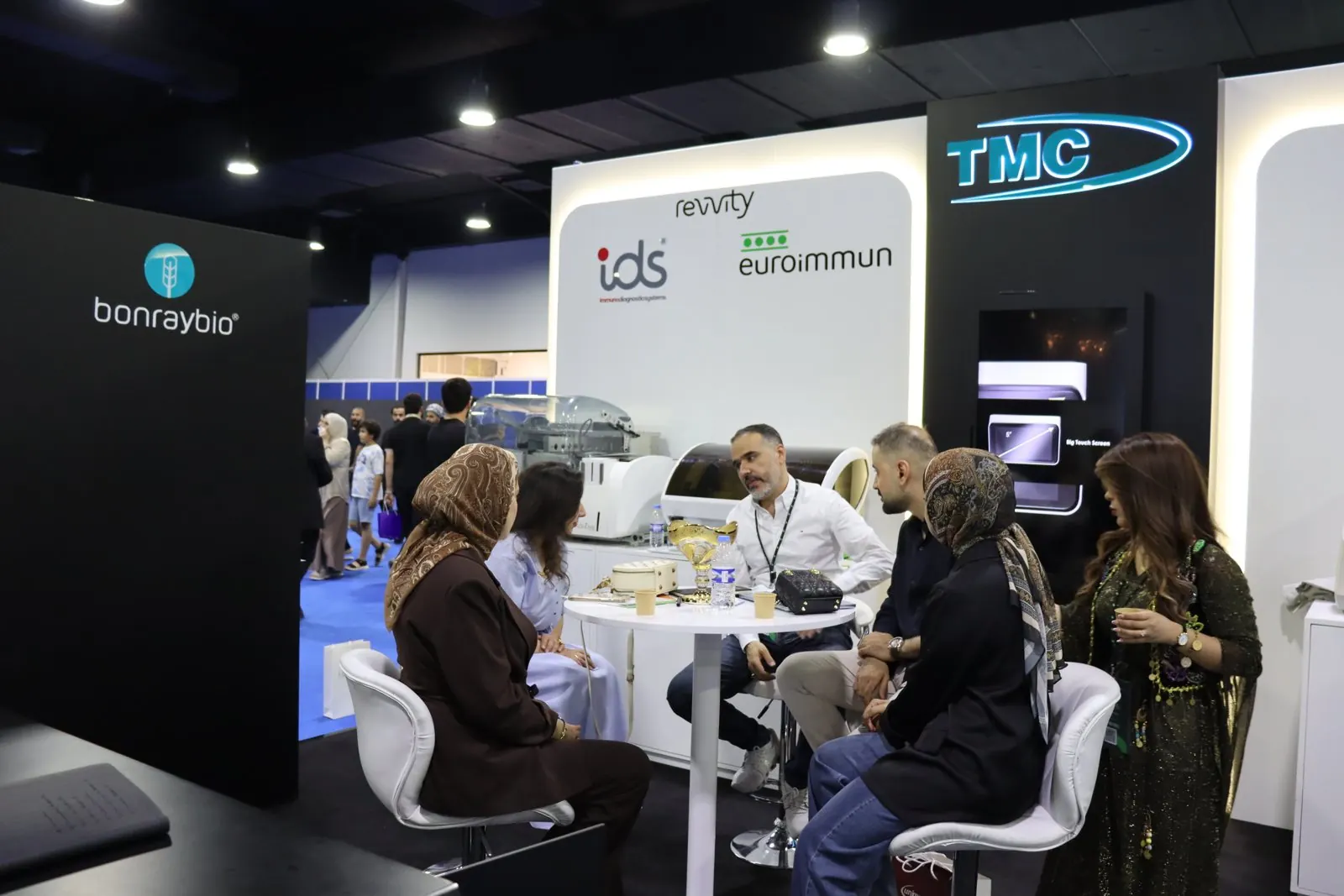 زوار وموظفون جالسون حول طاولة مستديرة أمام جدار Revvity IDS وEUROIMMUN