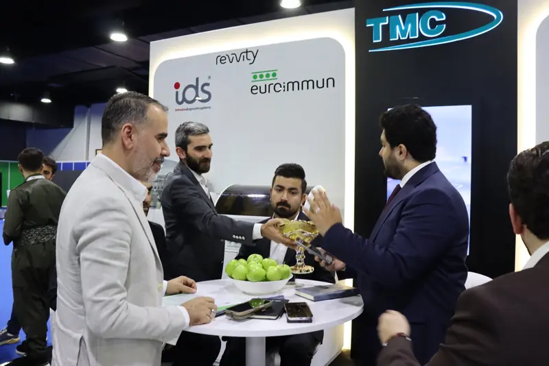 Group of men talking around a table at the stand under the TMC and EUROIMMUN signage