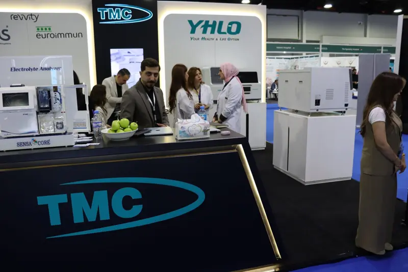 Laboratory professionals in white coats gathered around the TMC counter at MEDICO 2026